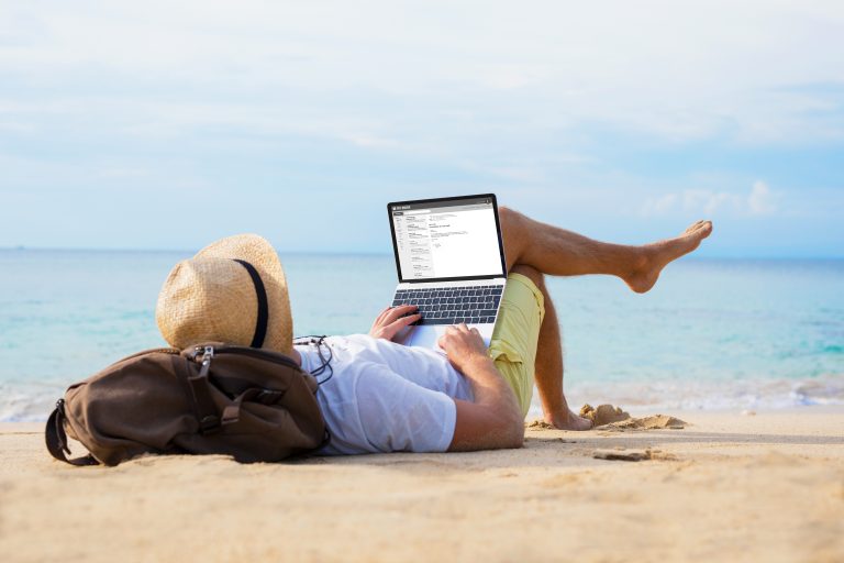 Homme sur une plage, allongé, travaille sur son ordinateur